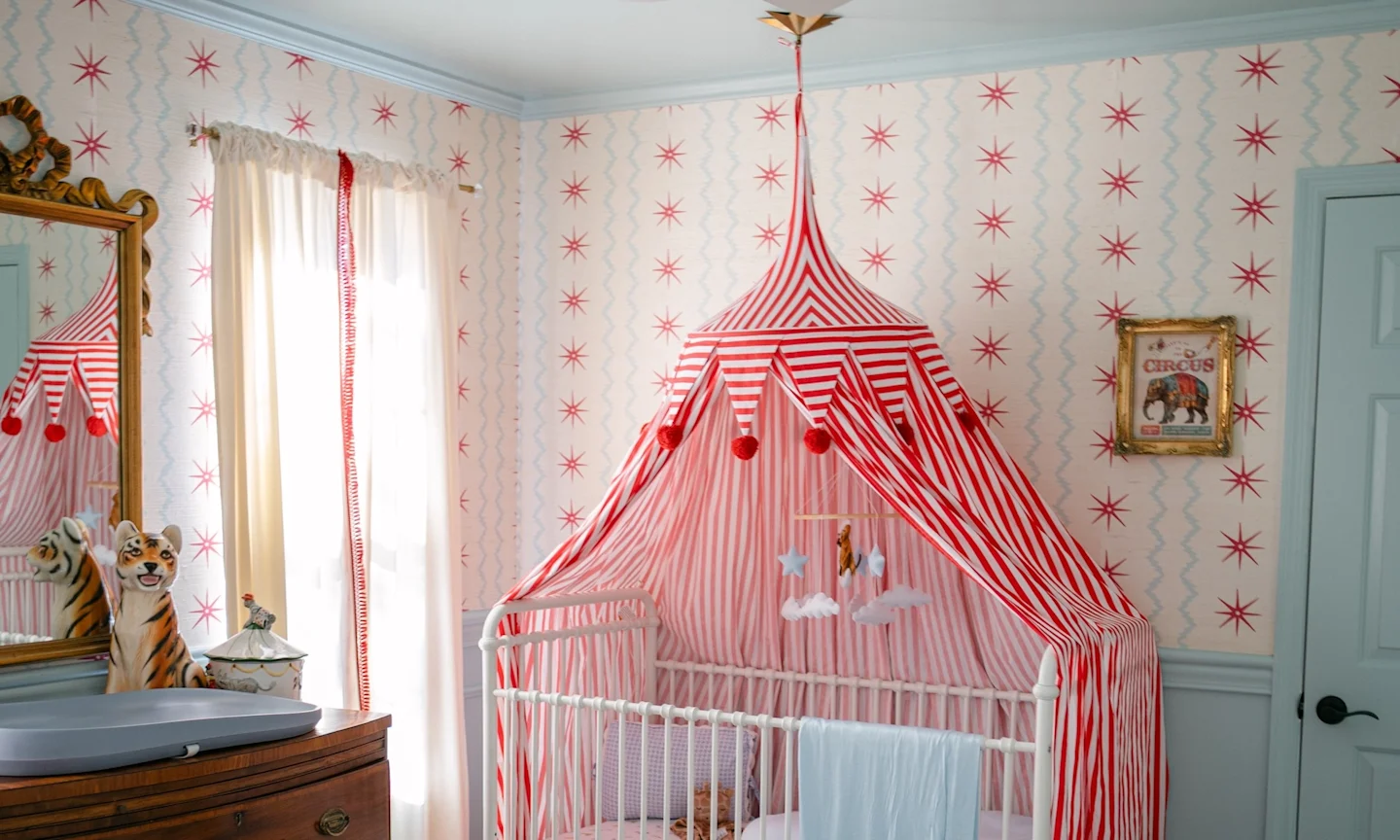 Crib with red and white striped circus-inspired canopy in a nursery.