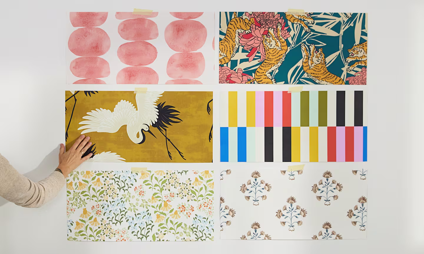 Person assessing 6 peel and stick wallpaper swatches on the wall.