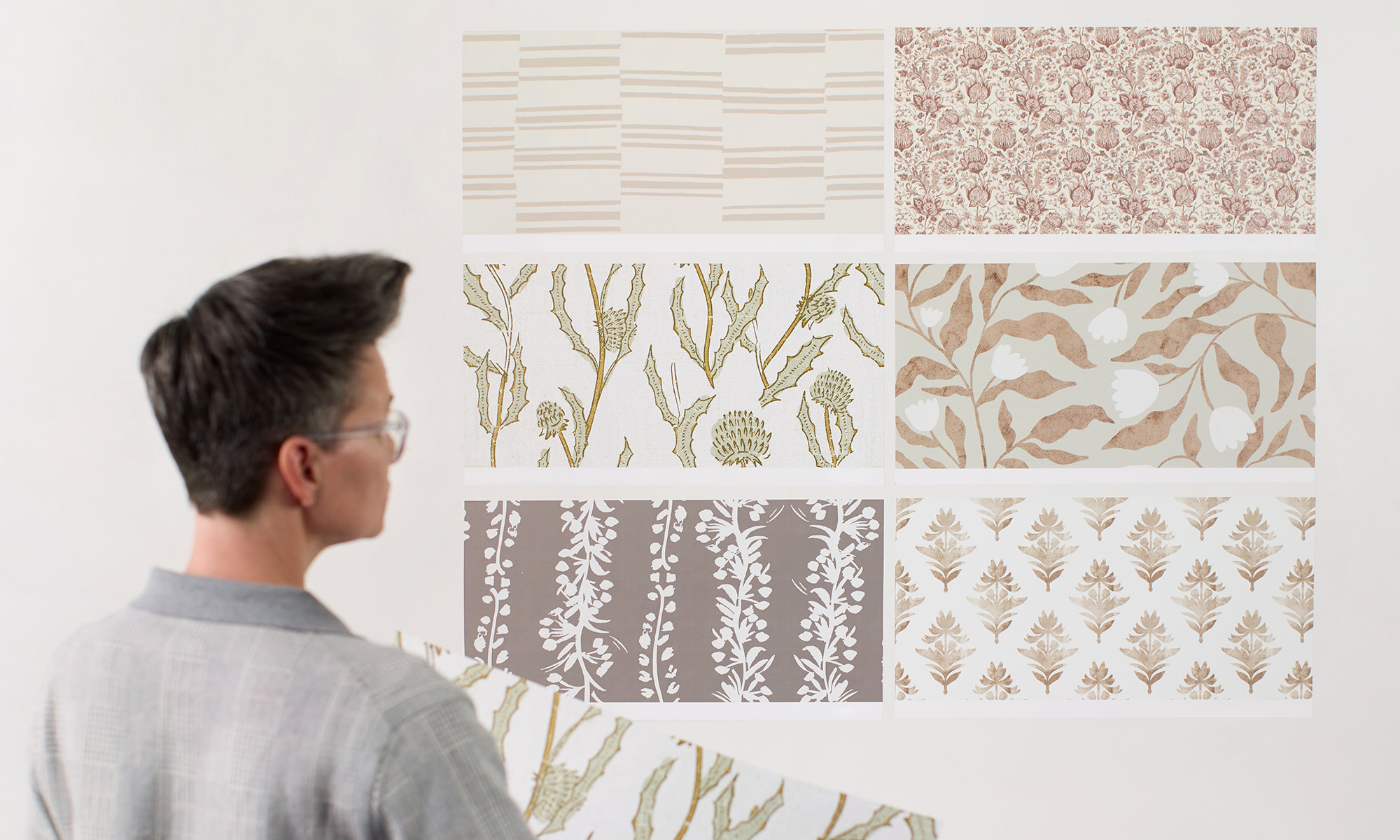 Person assessing 6 peel and stick wallpaper swatches on the wall.