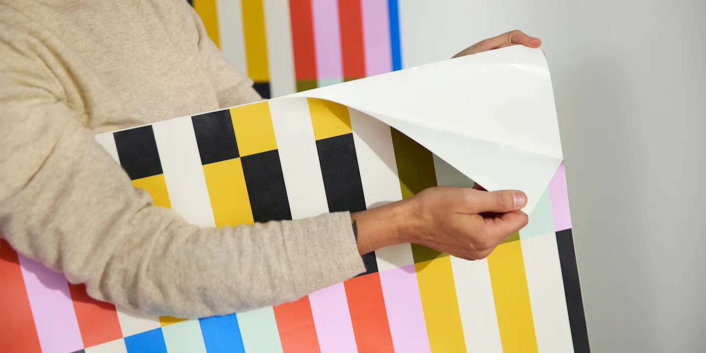 Hands peeling apart peel and stick wallpaper.