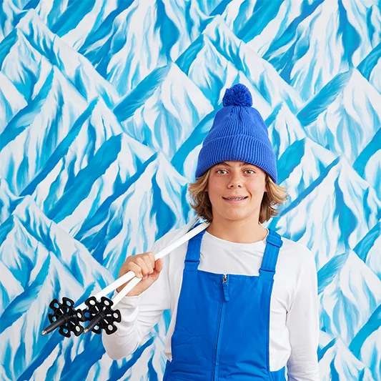 Boy in ski gear next to blue mountain wallpaper.
