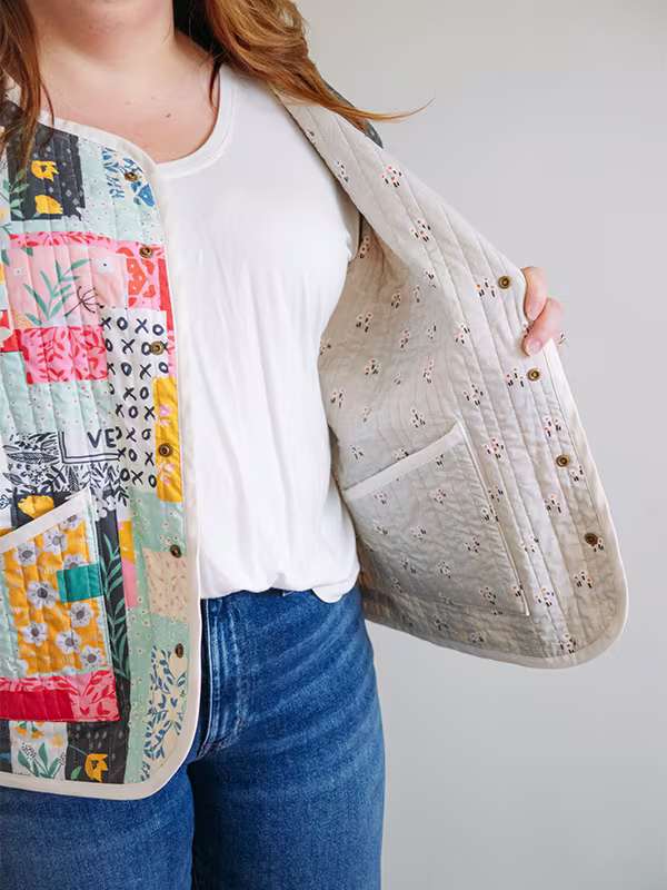 A close up of the white print with small red flowers inside Meg’s cheater quilt quilted jacket featuring delicate florals, most with a blue or pink theme. She is standing in front of a white wall.