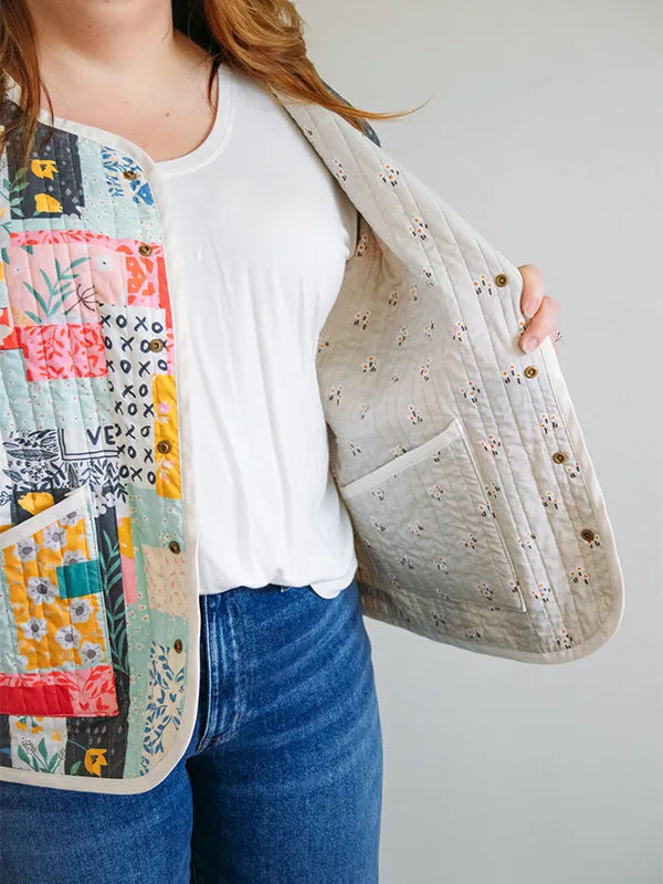 A close up of the white print with small red flowers inside Meg’s cheater quilt quilted jacket featuring delicate florals, most with a blue or pink theme. She is standing in front of a white wall.
