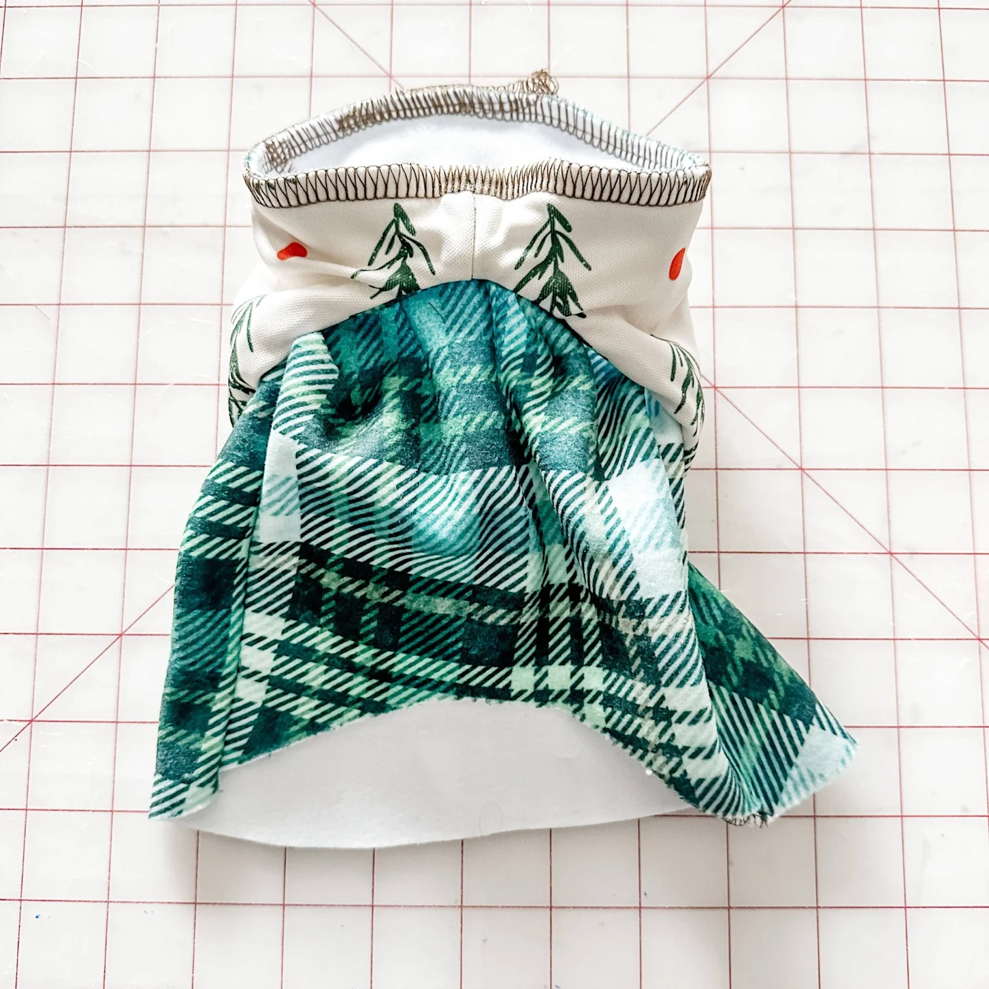 The hoodie and bodice are now sewn together and lay on a grid surface. The interior of the hoodie faces up, showing stitches that replace the sewing clips.