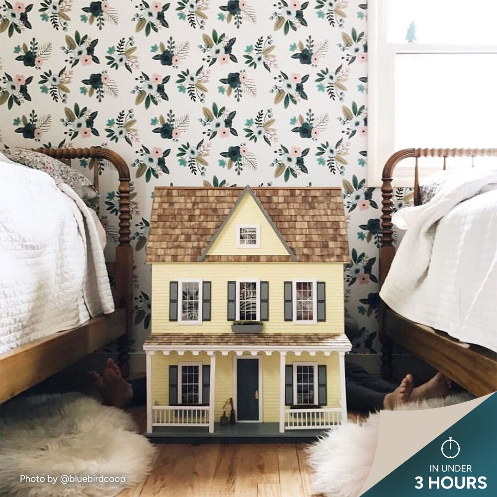 Dollhouse between two beds with floral wallpaper.