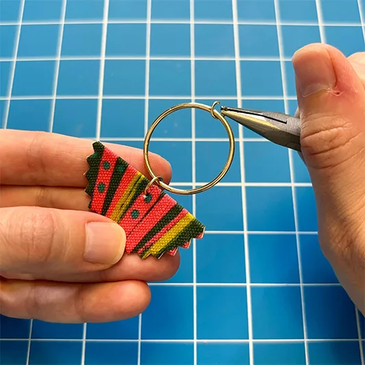 Hands using tool to bend a hoop around a fabric earring.