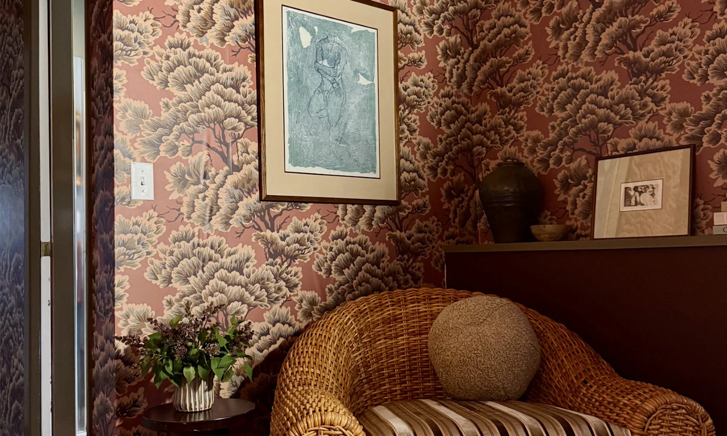 Office space with mauve tree wallpaper and a ratan chair.