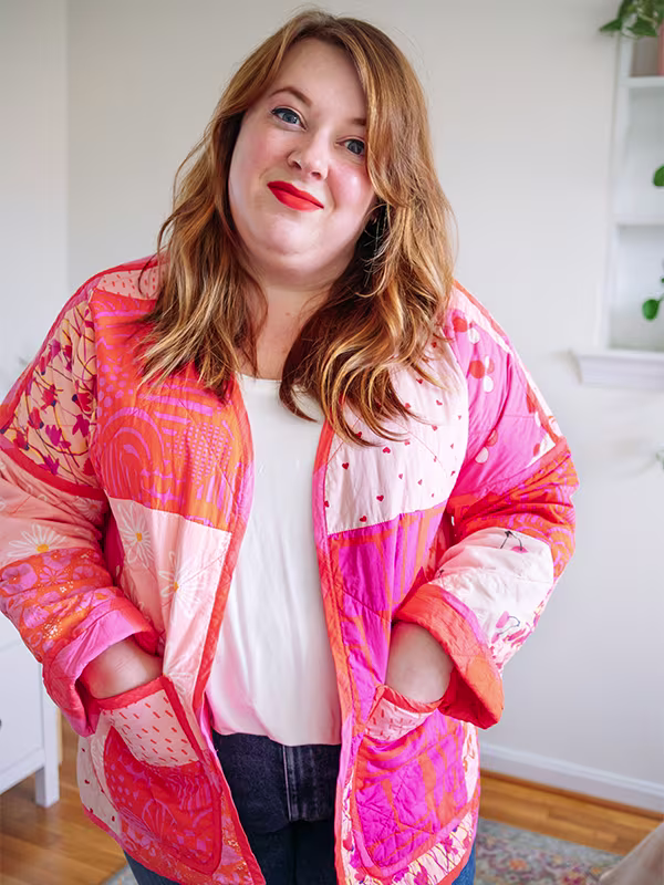 A close up of Meg's cheater quilt quilted jacket featuring pink prints and delicate florals. She is standing in front of a white wall.