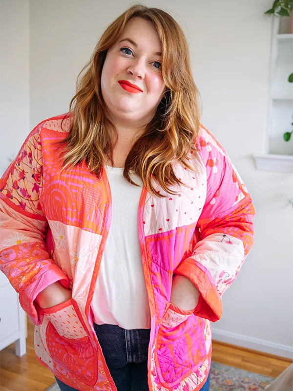 A close up of Meg's cheater quilt quilted jacket featuring pink prints and delicate florals. She is standing in front of a white wall.