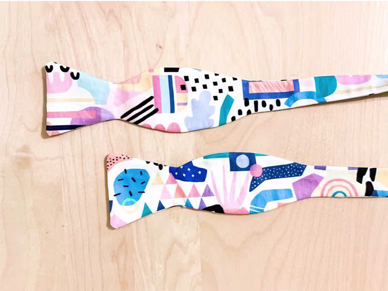 The ends of a bow tie lay on a wooden surface.