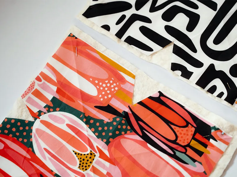 A close up of two cut-out fabric pieces lie next to each other and design side up on a white surface. Each piece has two diagonal creases pressed into it, one going top left to bottom right and one going top right to bottom left, to make an “X” shape. Eac