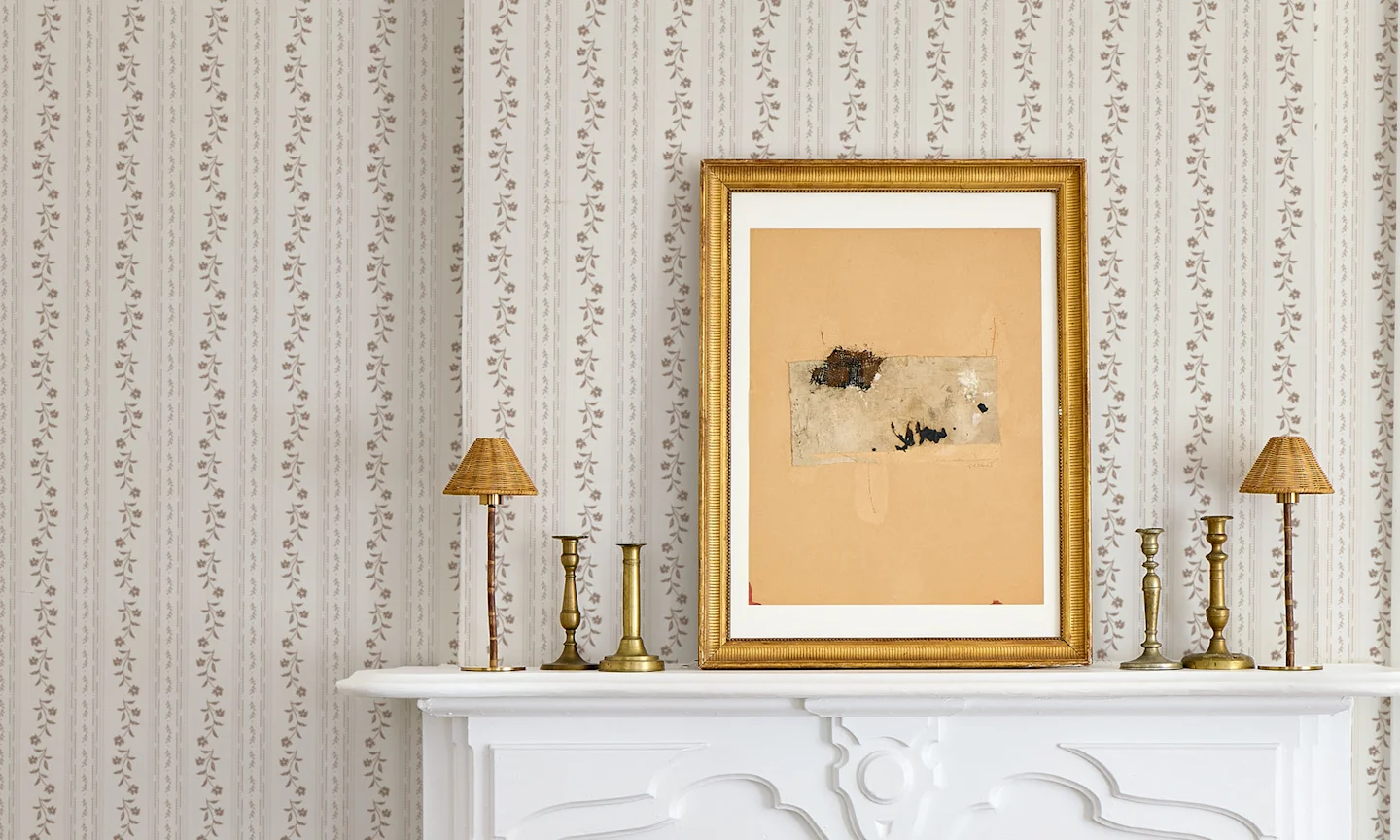A photo of an elegant mantle with brass artwork and accents, with a neutral floral stripe wallpaper