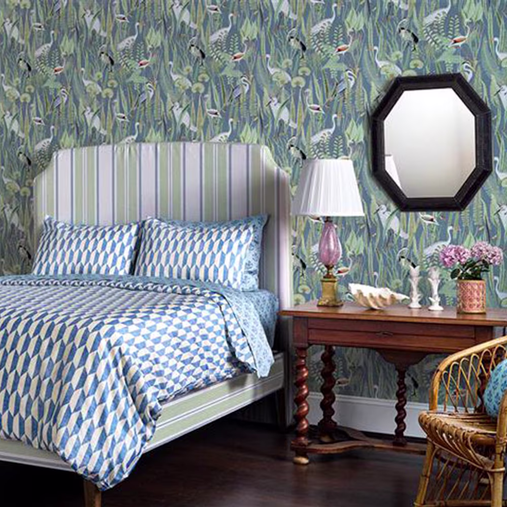 Bedroom with heron wallpaper, blue and white geometric bedding and a headboard upholstered in green stripes fabric.