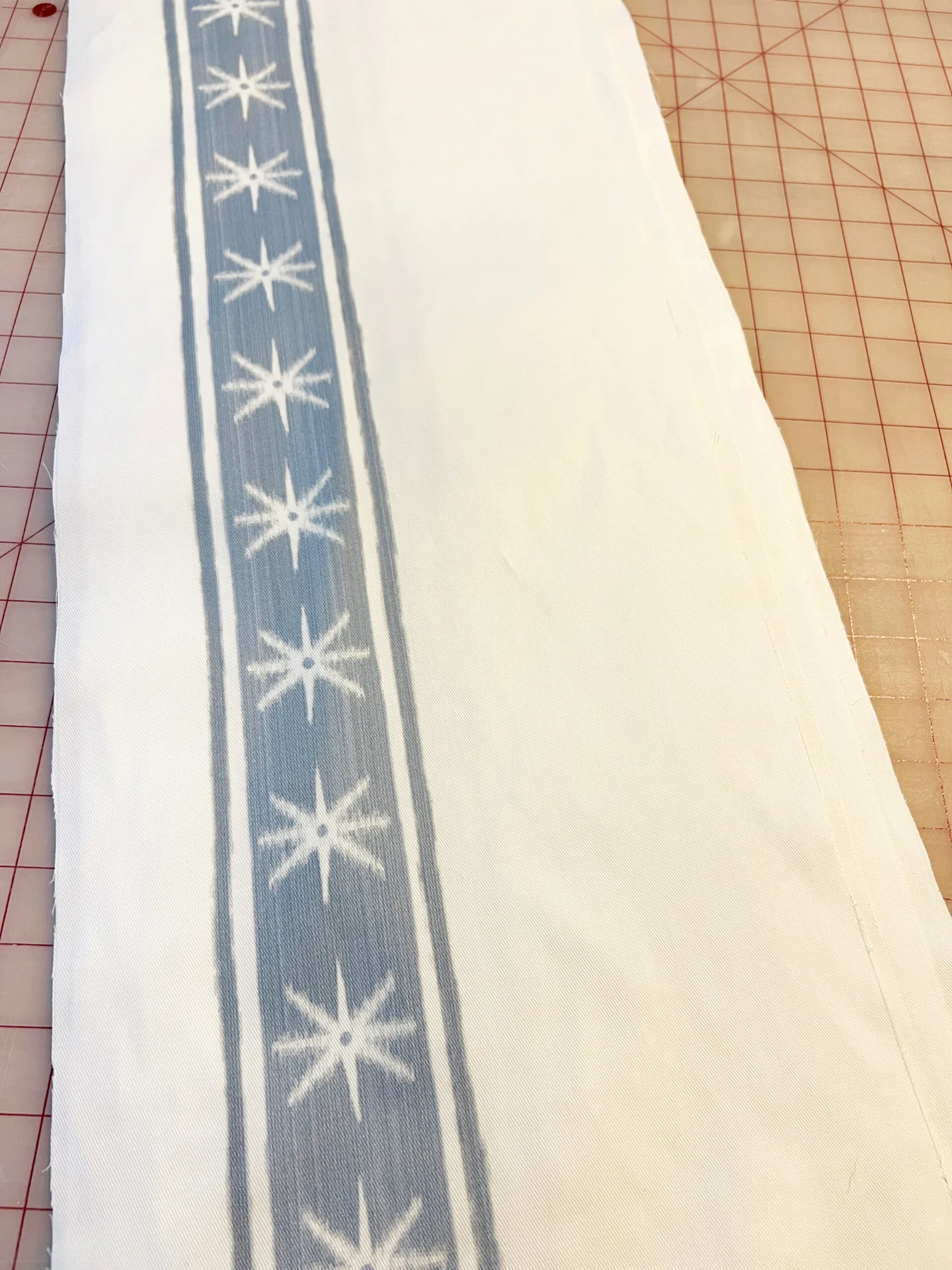 A close up of a strip of white fabric with a vertical thick blue stripe with white stars. A thin blue stripe appears on either side of each thicker stripe.