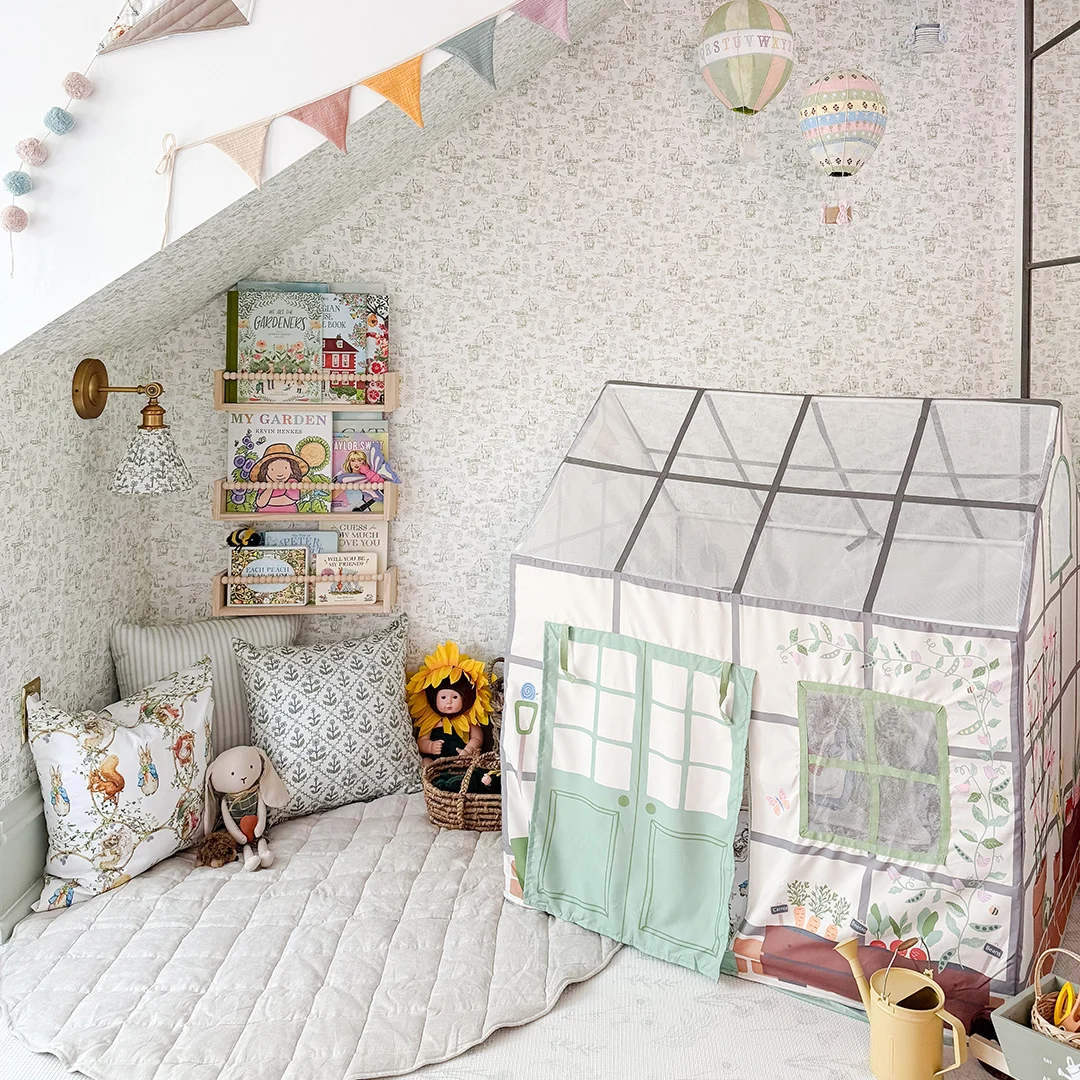Cozy nursery nook with soft floral wallpaper, fabric playhouse, children's books, bunting, and plush toys.