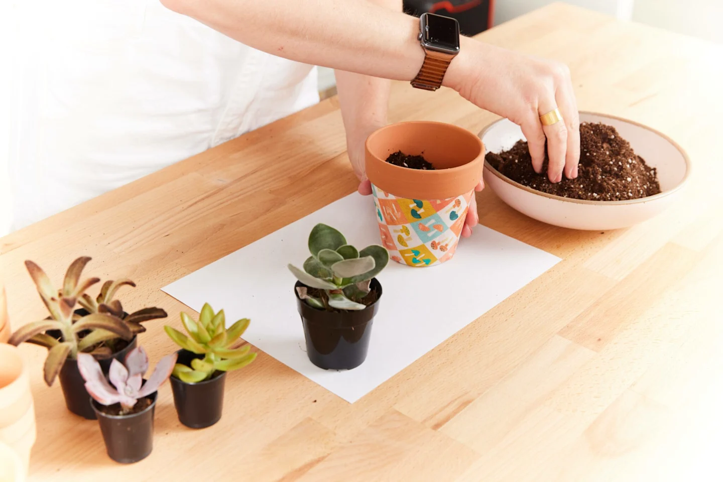 Alexa adds soil to the fully dried terracotta flower pot covered with fabric featuring small squares of small mushrooms in blue, white, green and peach.