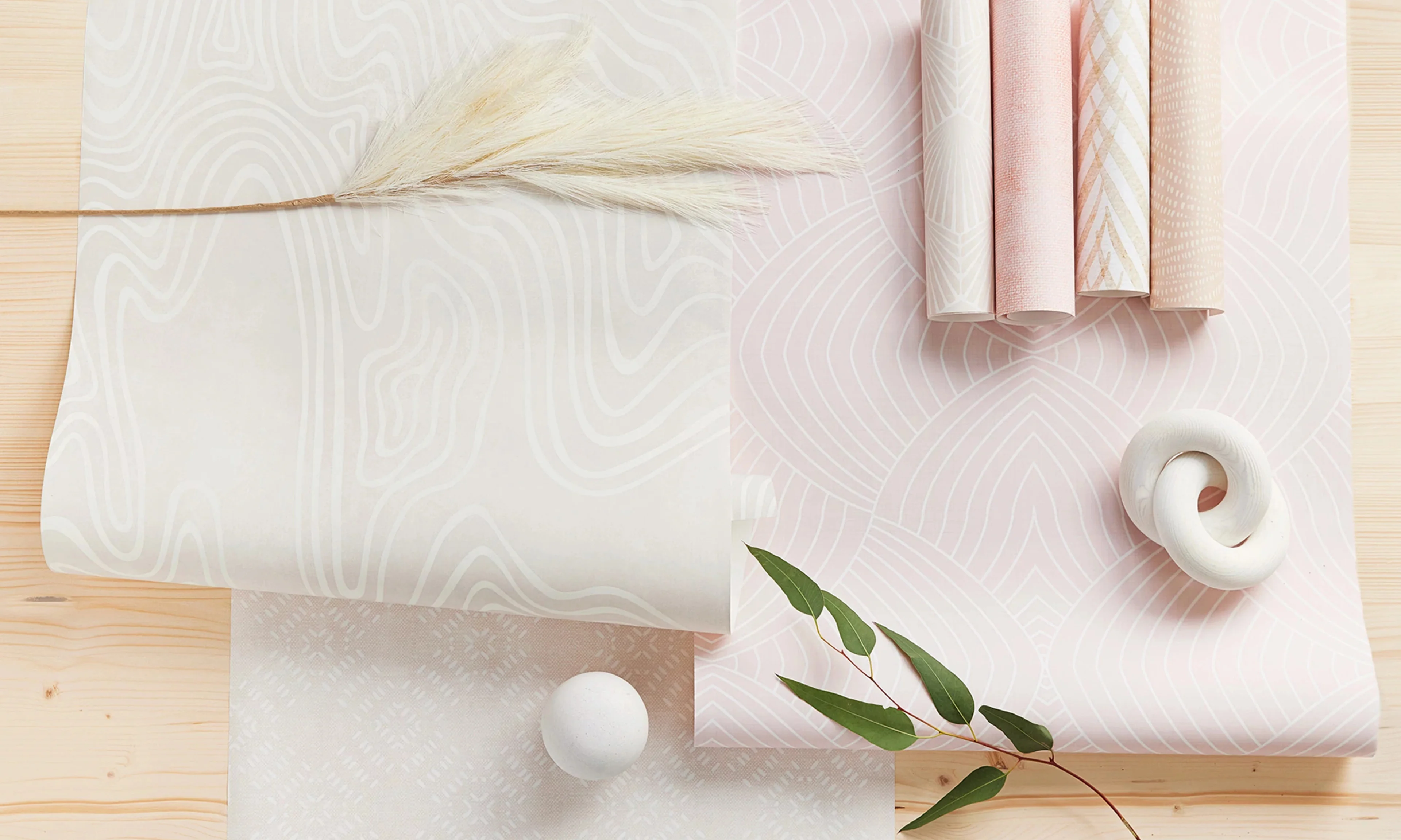 Pink and neutral wallpaper with subtle patterns printed on wallpaper rolls and swatches.