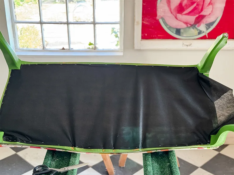 The bottom of the settee is facing up where a black dust cloth is stapled to the bottom.