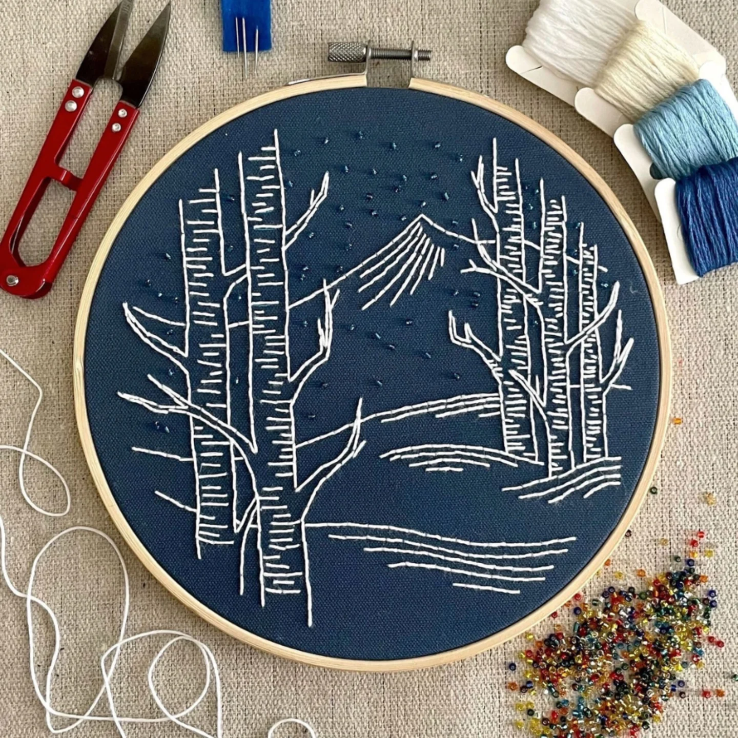 Fabric in embroidery hoop with tree & mountain design.