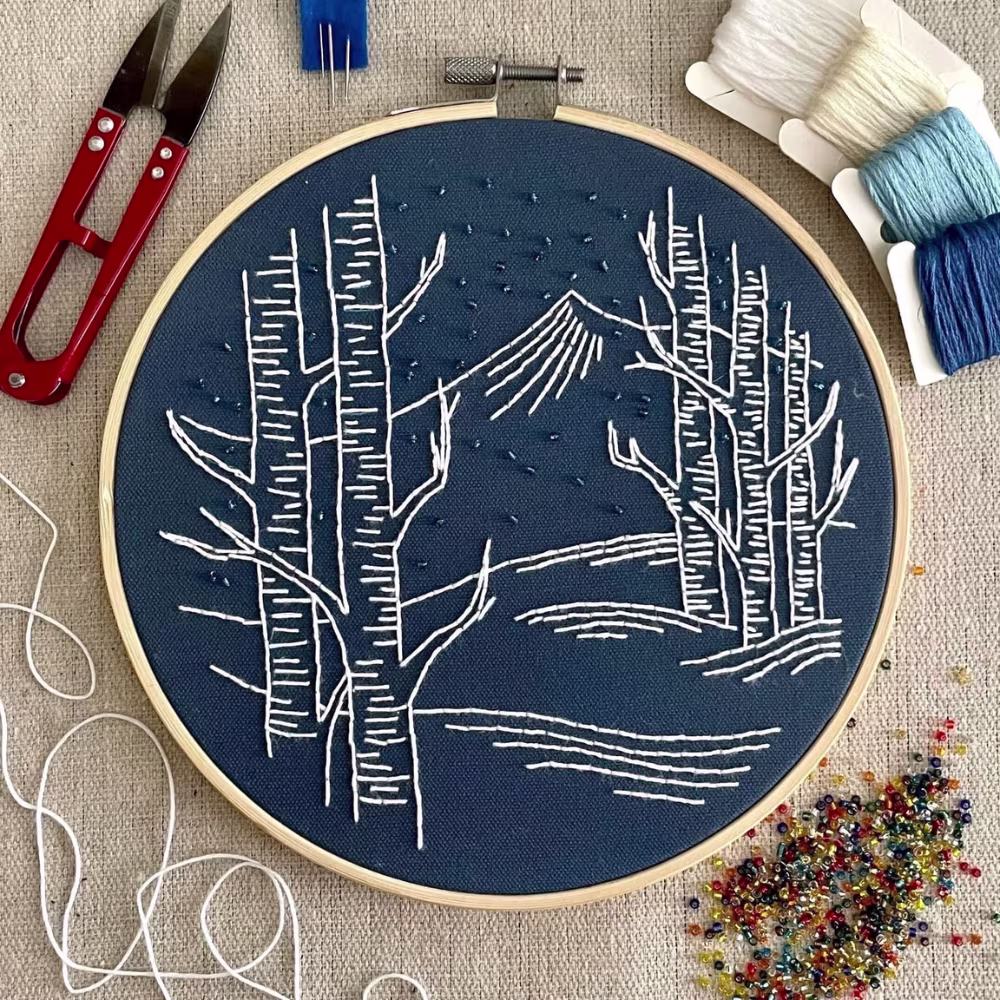 Fabric in embroidery hoop with tree & mountain design.