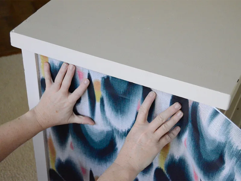 Barb places the wallpaper on the side of the dresses to measure how wide it needs to be.