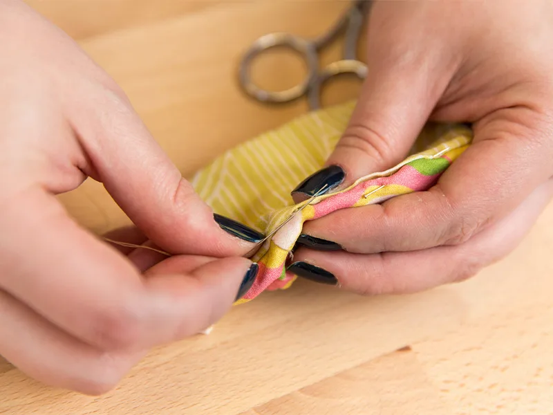 A women hand sews the opening of a baby shoe closed.