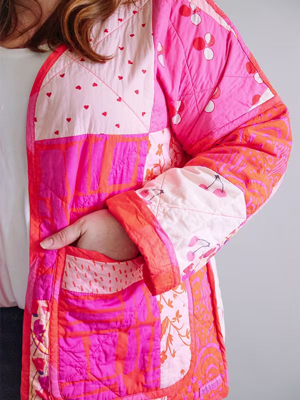 A close up of the left sleeve and front pocket of Meg’s cheater quilt quilted jacket featuring pink prints and delicate florals. She is standing in front of a white wall.
