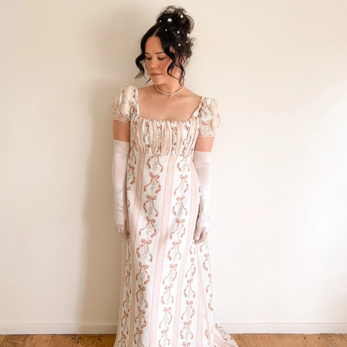 a woman in a Jane Eyre - era dress stands against a wall.