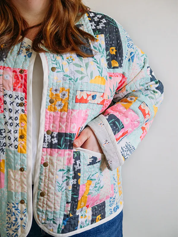 A close up of the left sleeve and front pocket of Meg’s cheater quilt quilted jacket featuring delicate florals, most with a blue or pink theme. She is standing in front of a white wall.