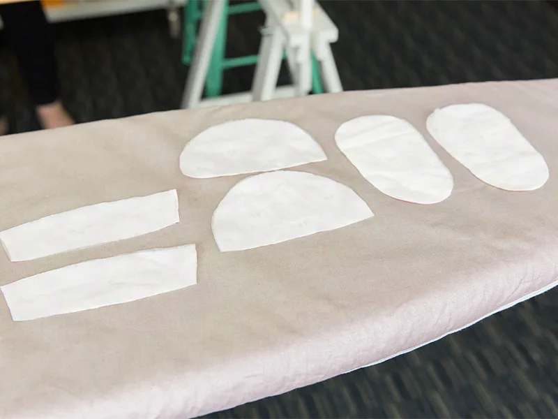 Six white pieces of interfacing lay on an ironing board.