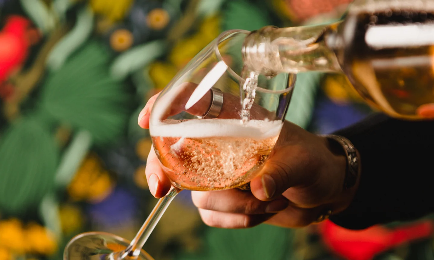 Handing pouring a glass of wine in front of a wallpapered wall