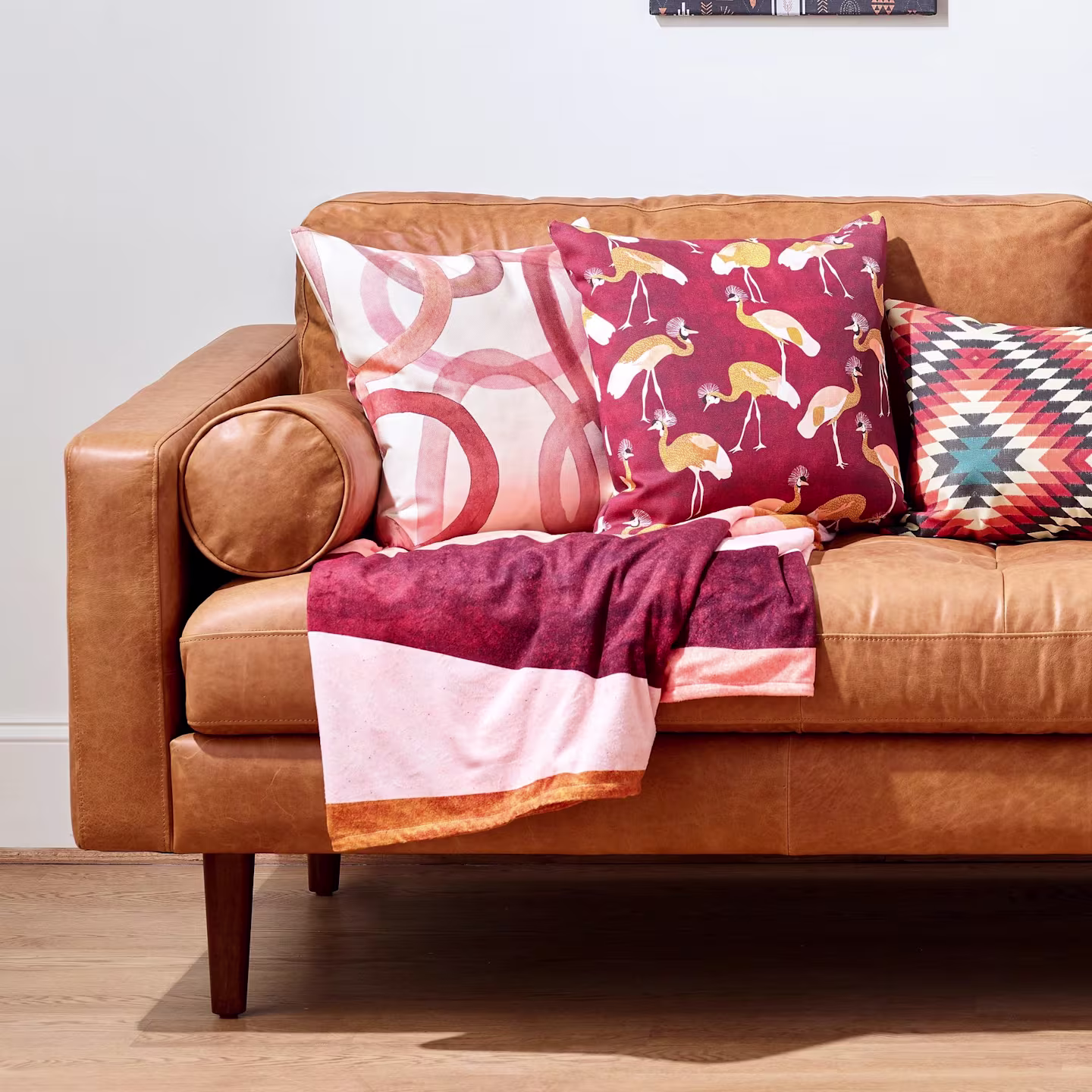 A minky throw blanket on a leather couch with coordinating warm-toned throw pillows
