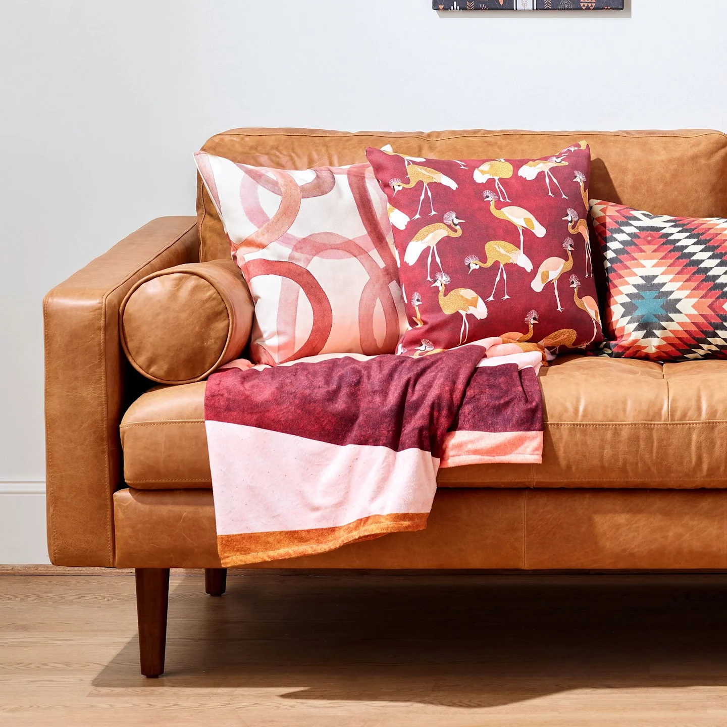 A minky throw blanket on a leather couch with coordinating warm-toned throw pillows