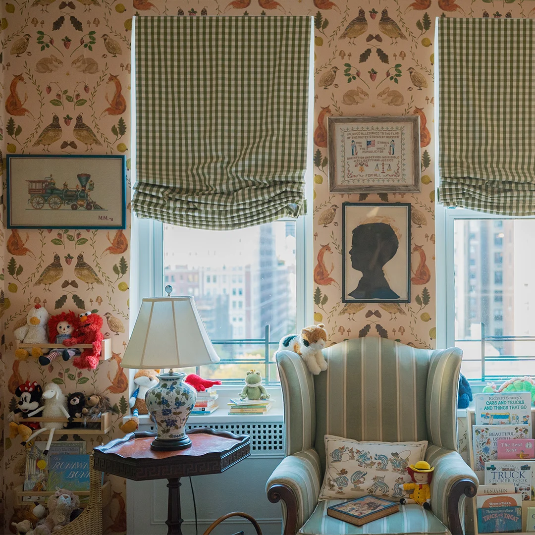 Reading corner with woodland animal wallpaper, green gingham shades, vintage furnishings, children's books, and plush toys.