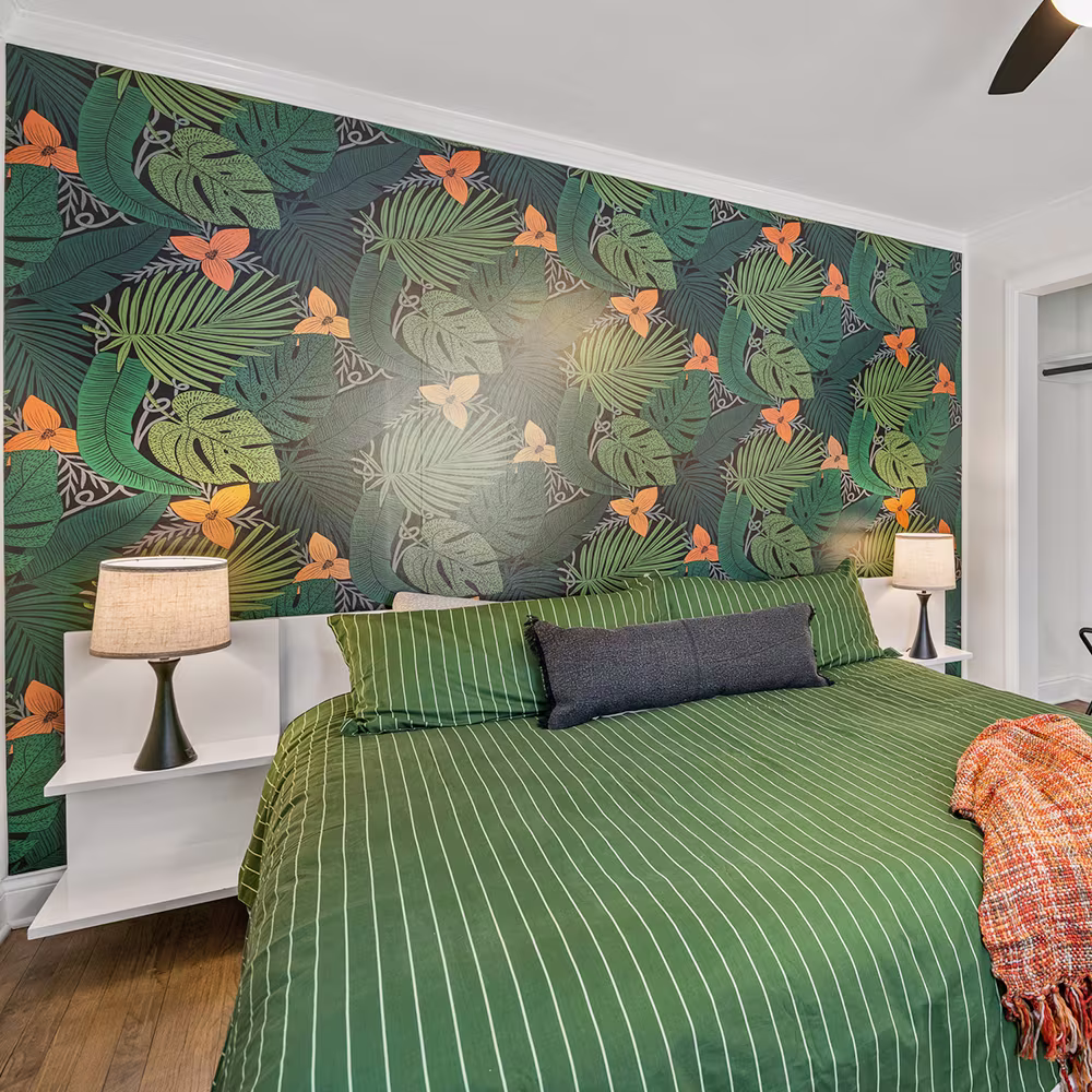 Bedroom with a moody tropical botanical design wallpapered behind the bed.