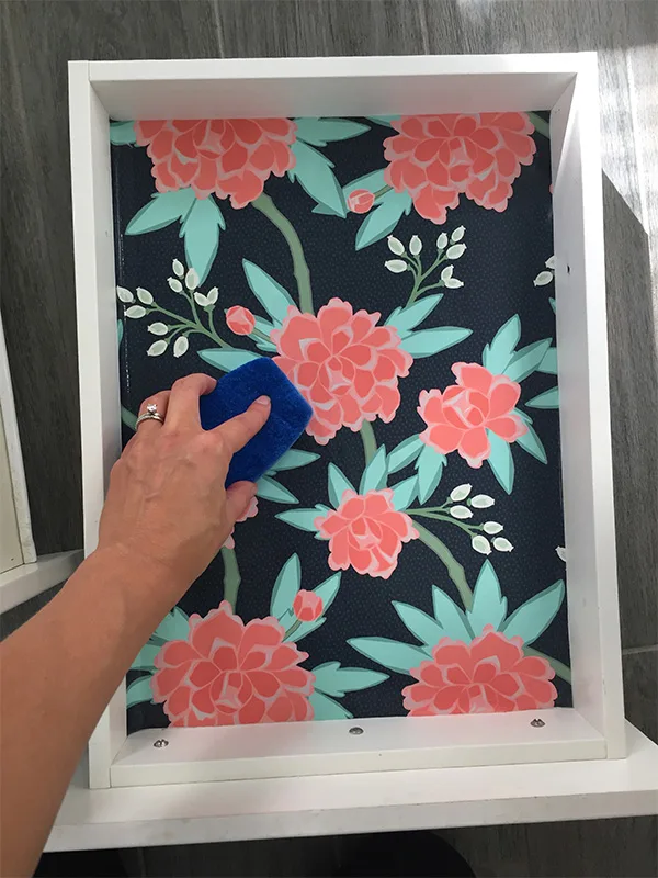 Suz rubbing a sponge over the wallpaper that is placed in a drawer.