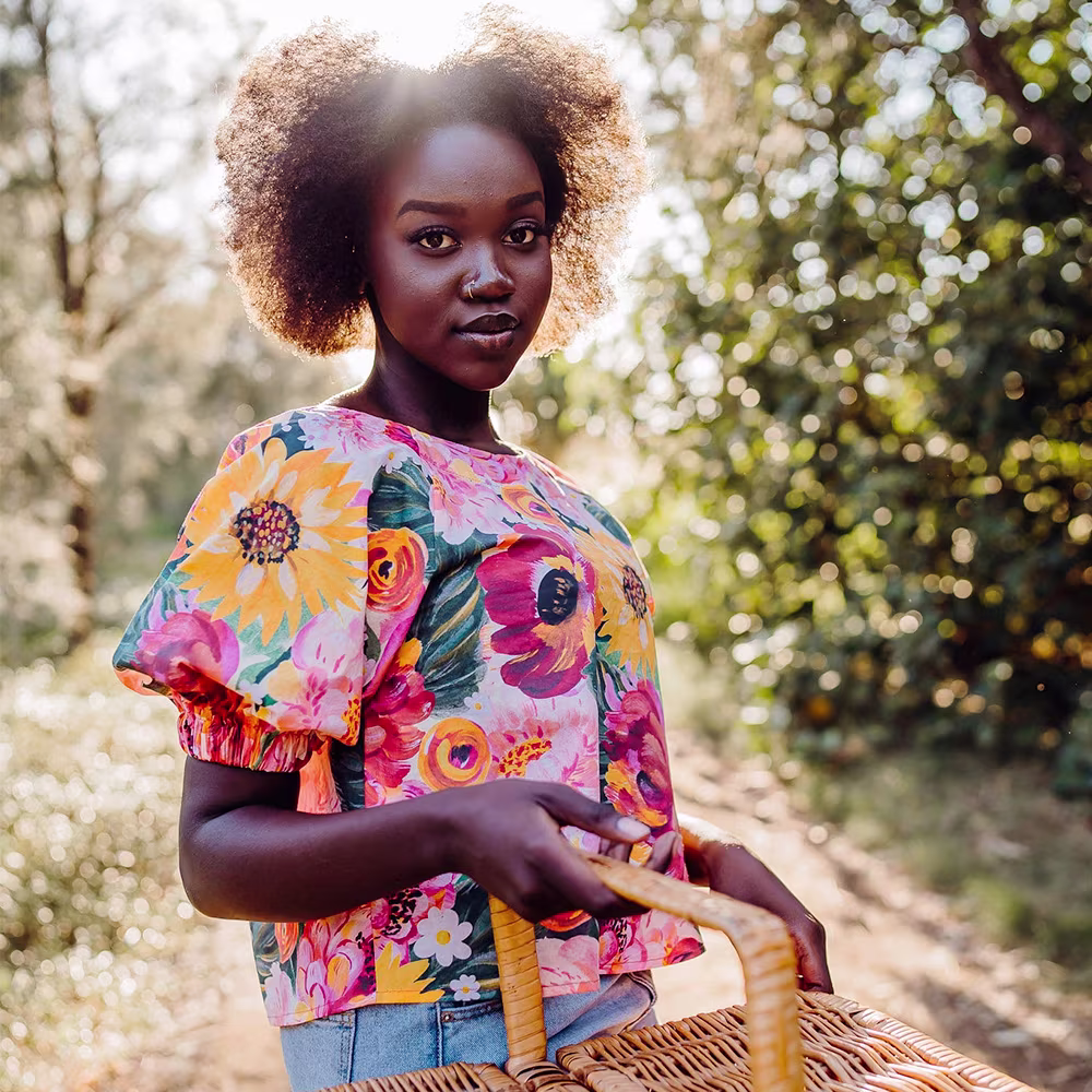 Woman in a floral blouse carrying a picnic basket in the woods.