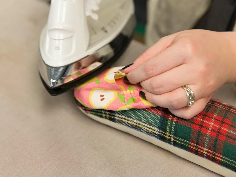 A women presses a baby shoe with an iron and tailor's cloth.