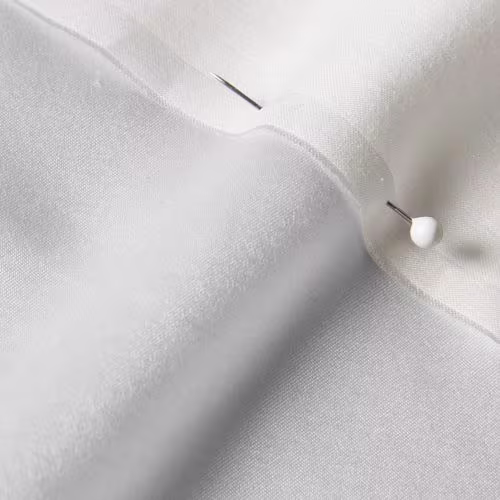 A close-up photo of white fabric with a pin running through it