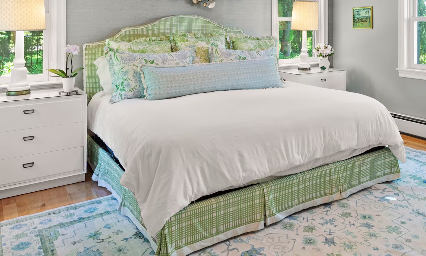 Bed with green upholstered headboard and skirt plus blue and green floral pillows.