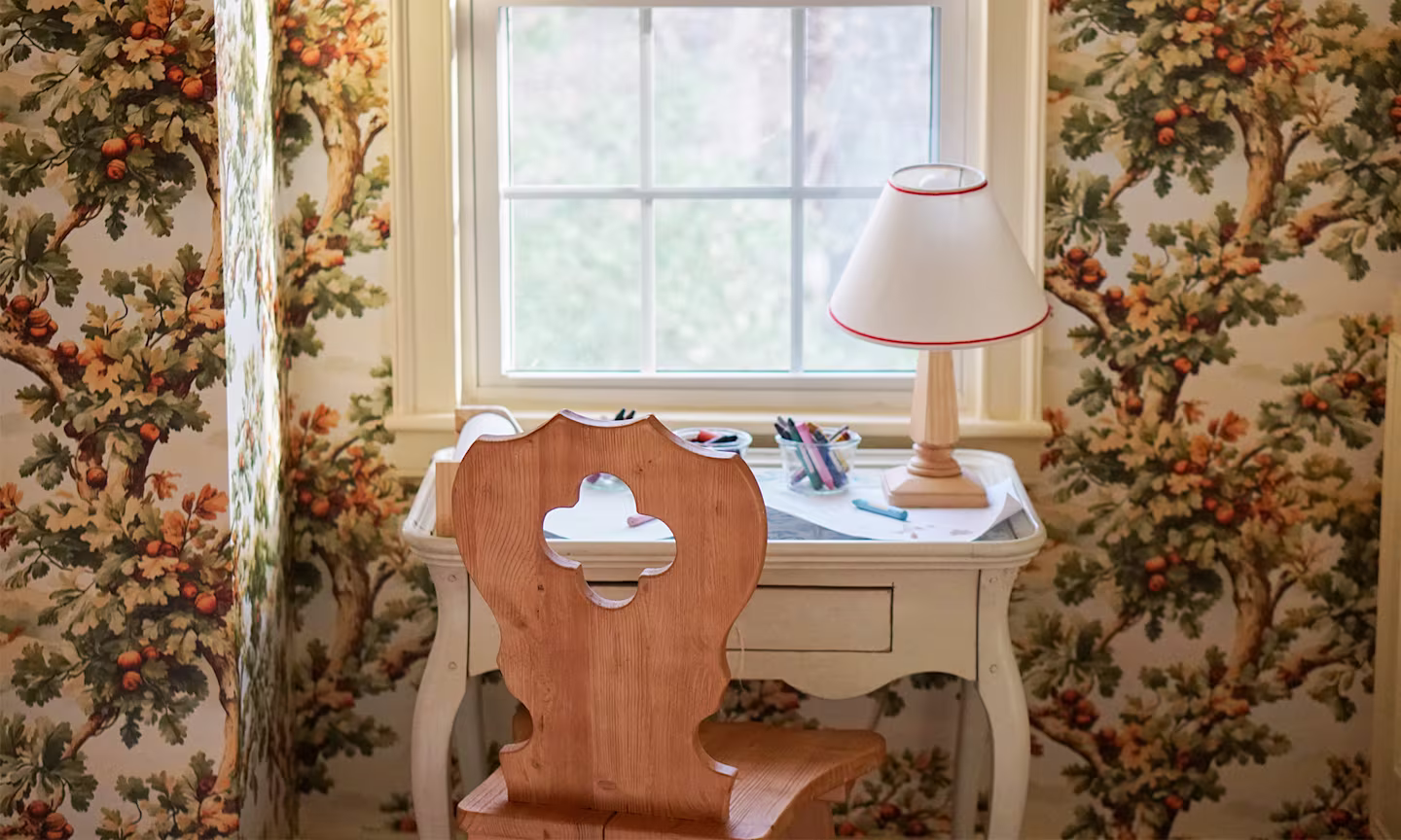 Childs desk in front of a window and wall with oak tree wallpaper.
