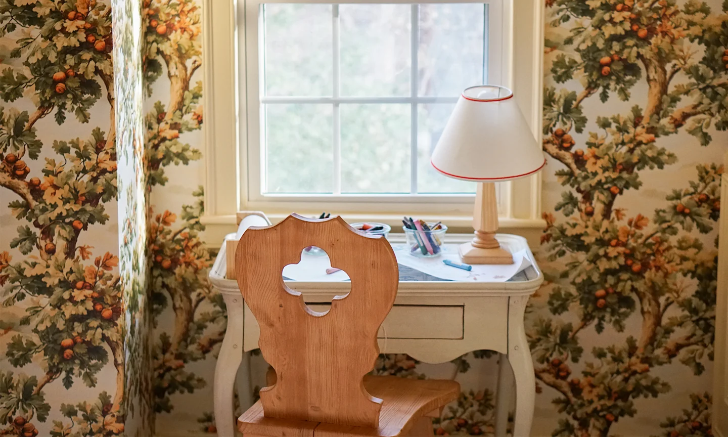 Childs desk in front of a window and wall with oak tree wallpaper.