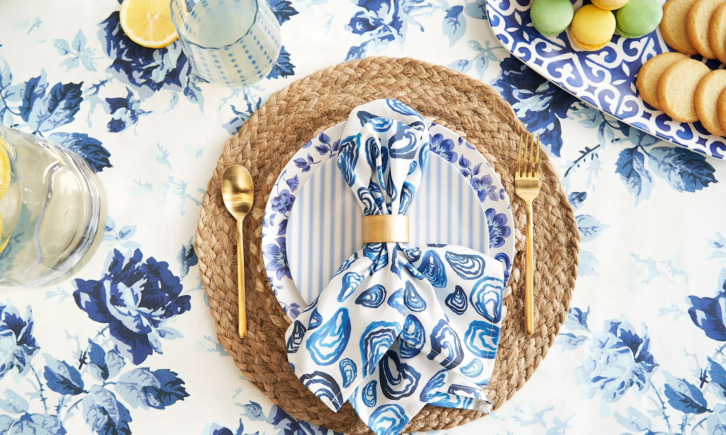 Table setting with a blue floral tablecloth and blue oyster dinner napkin.