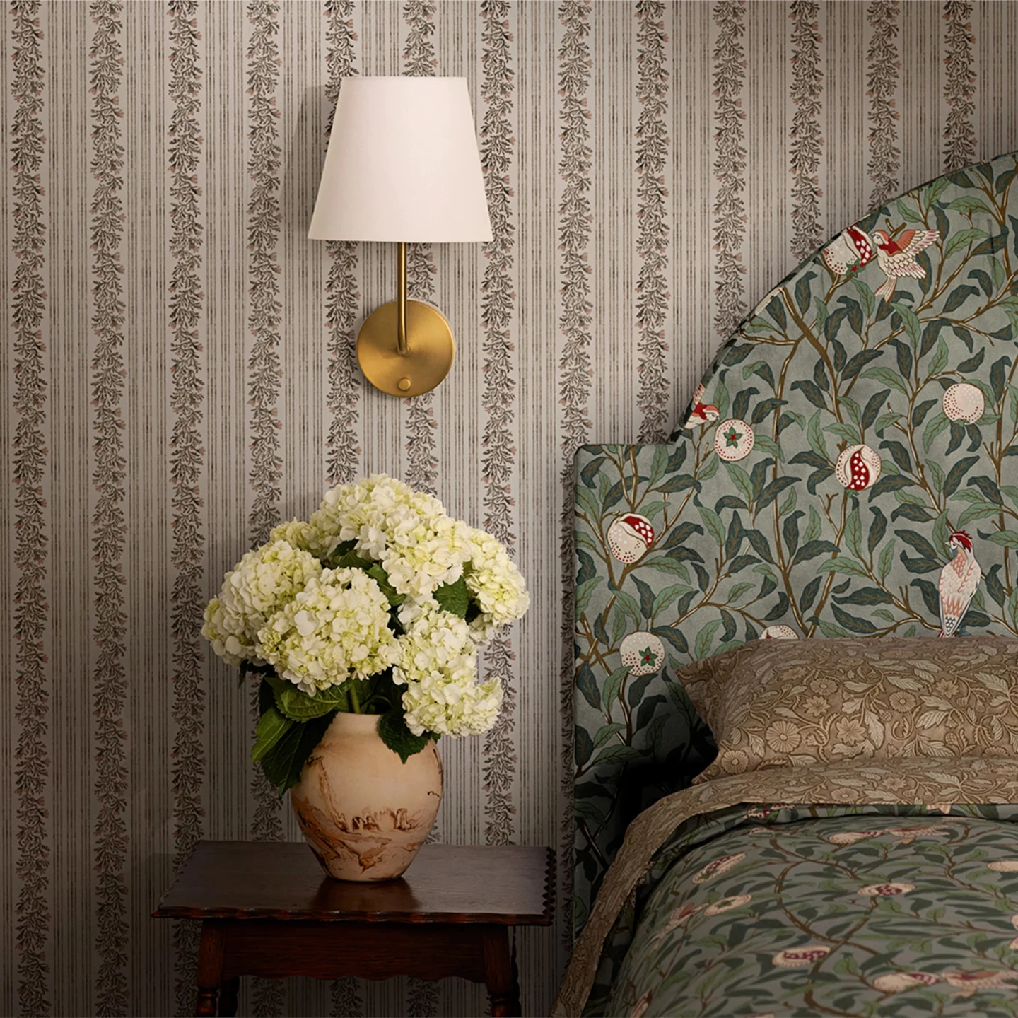 Tan floral stripe wallpaper and William Morris fig design on upholstered bed frame and duvet cover.
