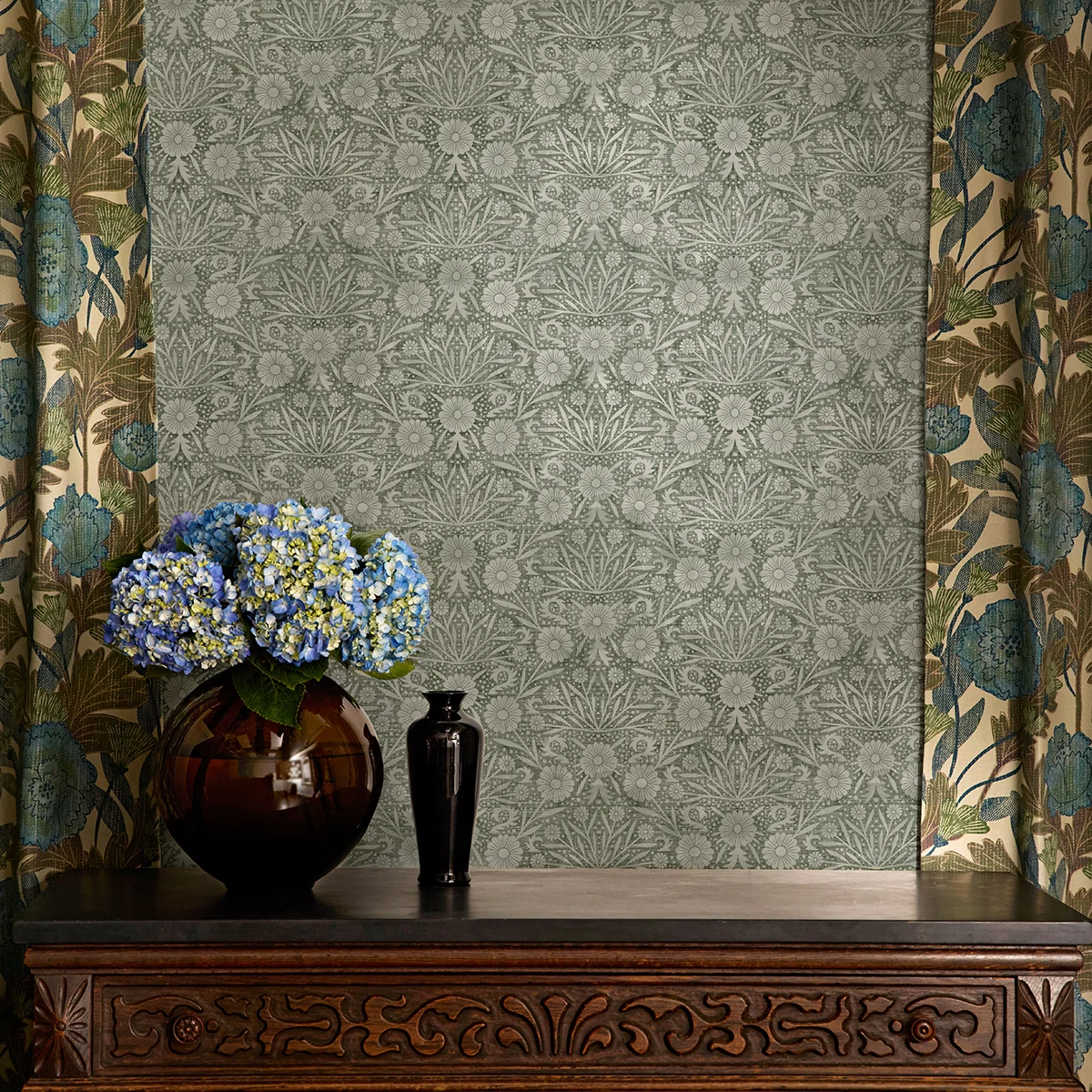 Green floral damask craft revival wallpaper and botanical curtains above a vintage table.