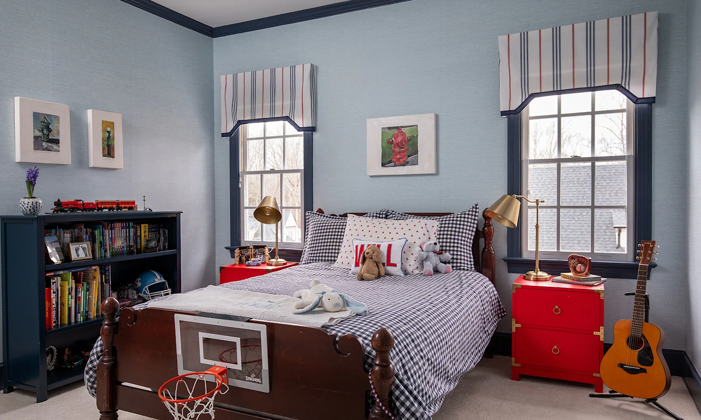 Boys bedroom with blue grasscloth wallpaper blue striped bedding and  curtains as well as red furniture.