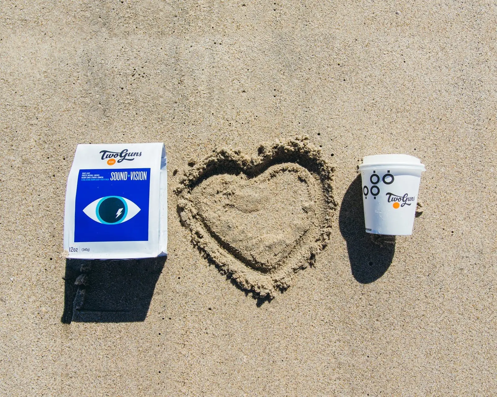 a coffee cup and bag of coffee on a sandy beach
