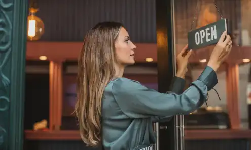 Woman hangs up an Open sign on the front door of a restaurant