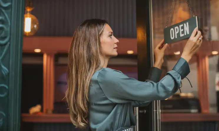 Woman hangs up an Open sign on the front door of a restaurant