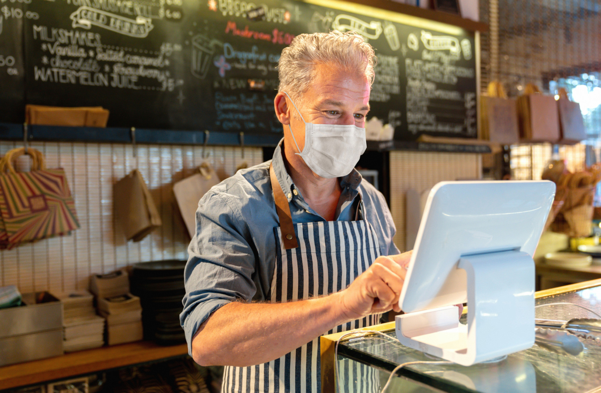 A restaurant owner using a tablet while wearing a mask